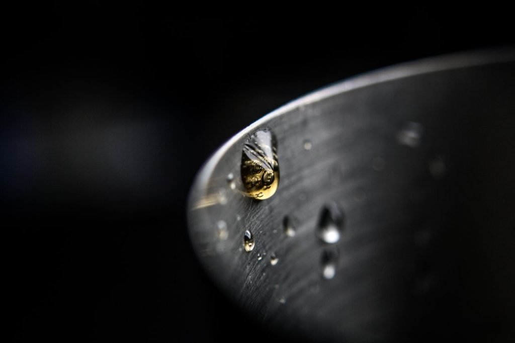Close-up macro image highlighting a waterdrop on a curved steel surface with a dark background.